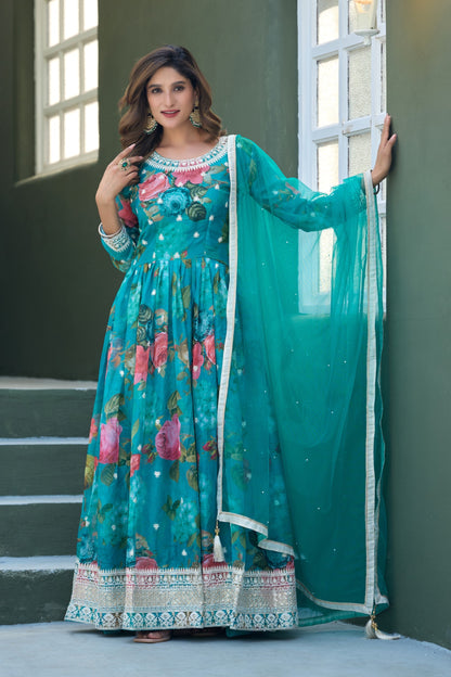 Woman in a teal floral dress with matching dupatta standing against a wall.